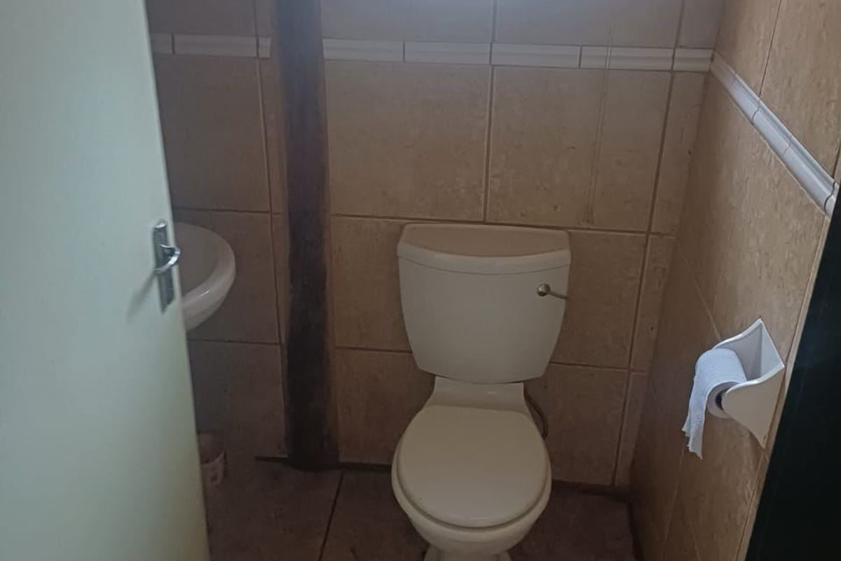 A compact guest bathroom featuring a standard toilet, wall-mounted basin, and tiled finishes, requiring cosmetic updates to improve its overall condition.