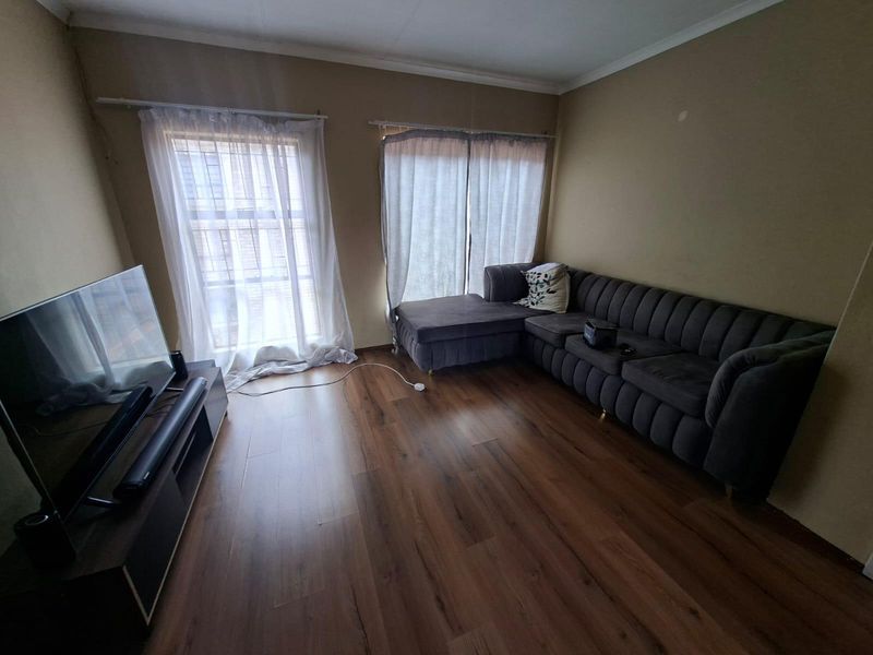 A living room featuring dark laminate flooring and dual windows with curtain rails, offering a neutral base for interior updates.