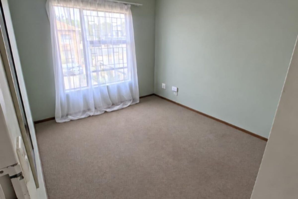 A clean, empty bedroom featuring neutral green walls, carpeted flooring, and a window fitted with security bars.