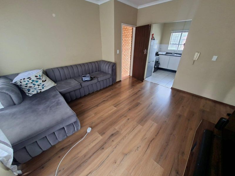 Open plan living area featuring laminate flooring and coved ceilings, with an adjacent kitchen area visible through the doorway.