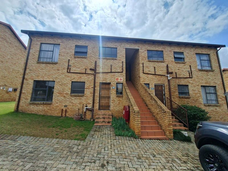 Front elevation of a two-story face brick apartment complex featuring external staircases, security gates, and paved driveway access.
