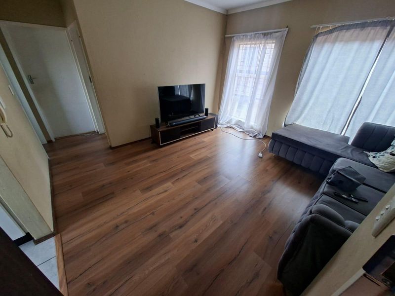A living room featuring warm-toned laminate flooring and neutral wall finishes, providing a functional and well-lit space.