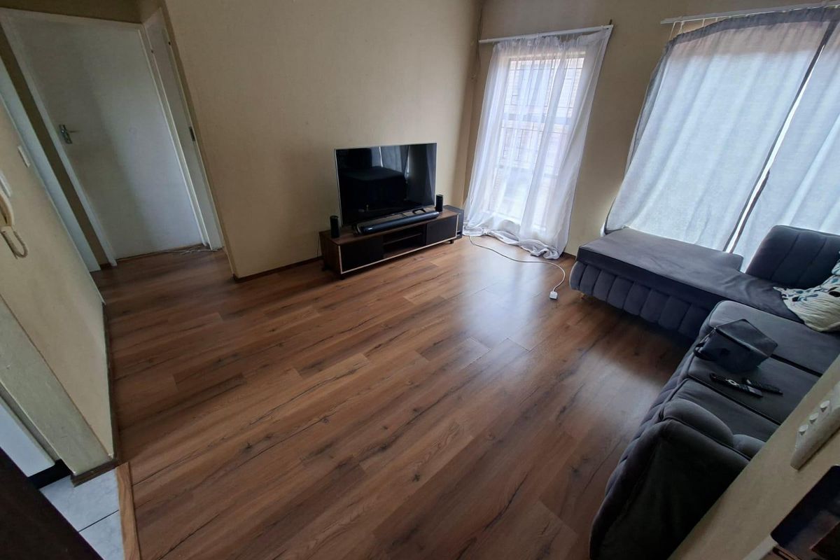 A living room featuring warm-toned laminate flooring and neutral wall finishes, providing a functional and well-lit space.