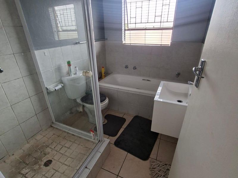 A functional bathroom featuring a separate shower enclosure, bathtub, and wall-mounted vanity basin with tiled finishes throughout.