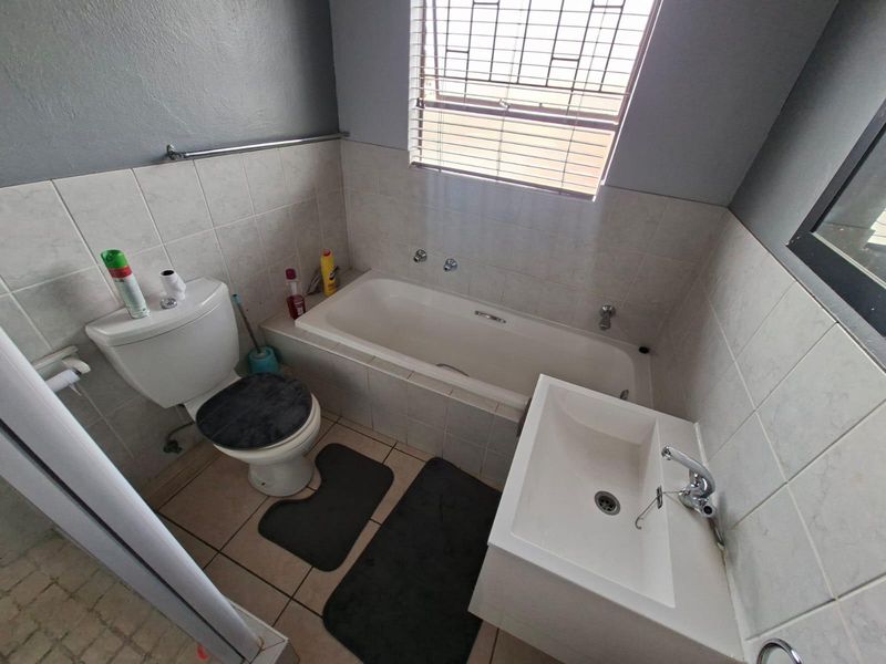 A functional bathroom featuring a bathtub, wall-mounted basin, and toilet with tiled splashbacks and neutral finishes.