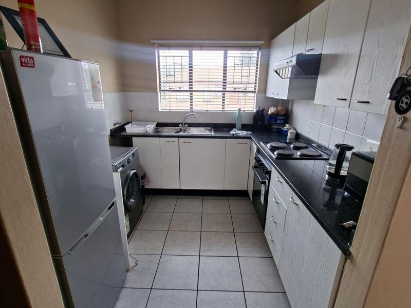 Functional kitchen featuring white cabinetry, black granite countertops, built-in oven and hob, and tiled flooring with a window providing natural light.
