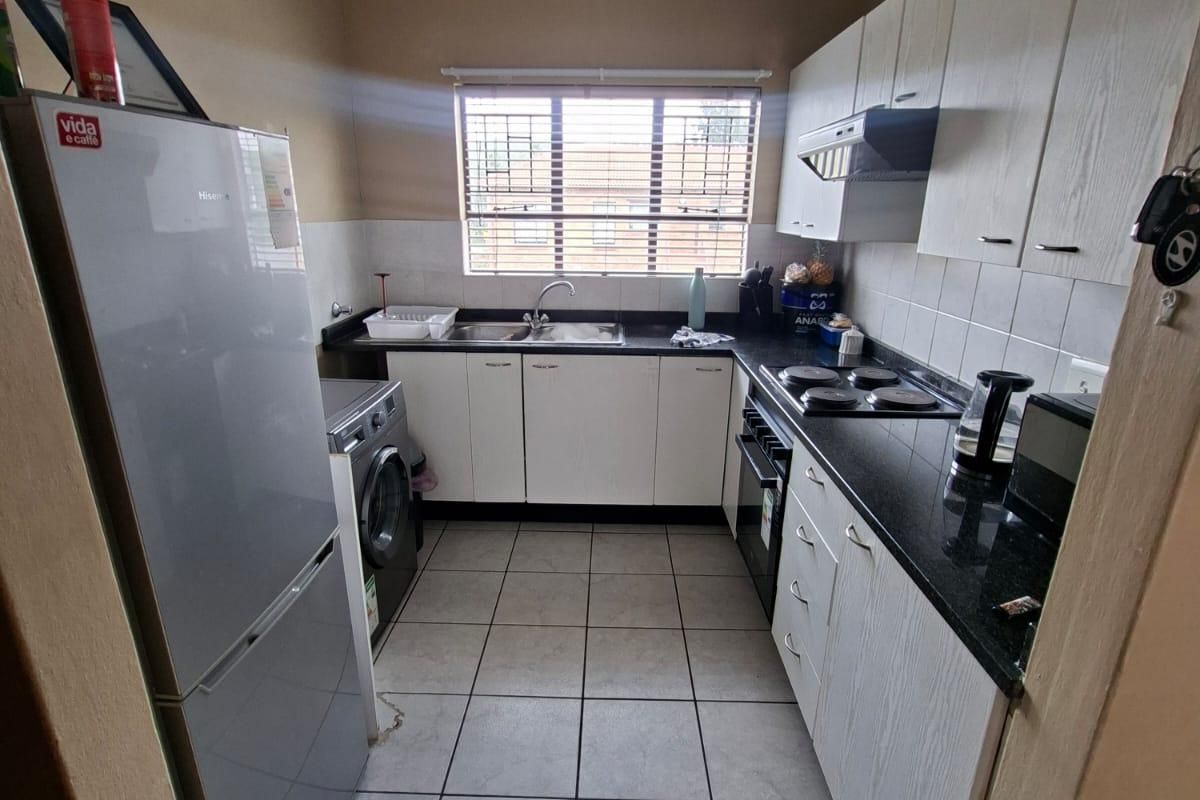 Functional kitchen featuring white cabinetry, black granite countertops, built-in oven and hob, and tiled flooring with a window providing natural light.
