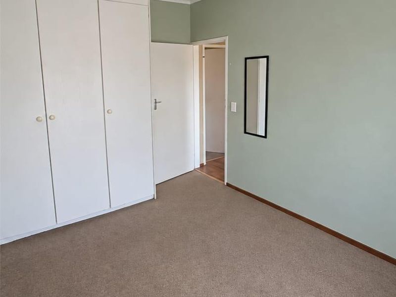 A clean, empty bedroom featuring neutral carpeted flooring, built-in cupboards, and a soft green accent wall.