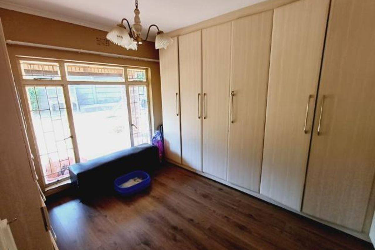 A bedroom featuring extensive built-in cupboards, laminate flooring, and a large window with security bars, providing ample storage and natural light.