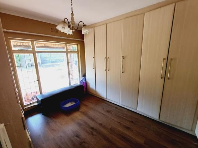 A bedroom featuring extensive built-in cupboards, laminate flooring, and a large window with security bars, providing ample storage and natural light.