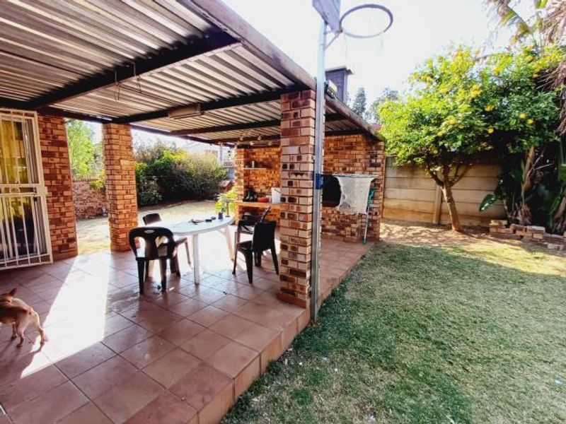Covered outdoor patio featuring brick pillars, tiled flooring, and a built-in brick braai, overlooking the garden area.