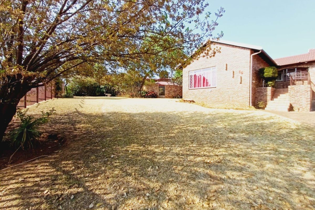 A spacious rear garden featuring a brick-faced house, mature trees, and a large lawn area with brick steps leading to the entrance.