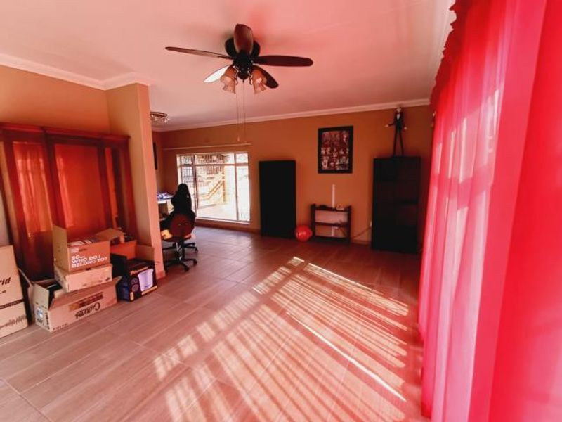 A spacious living area featuring tiled flooring and a ceiling fan, offering a versatile layout with natural light.
