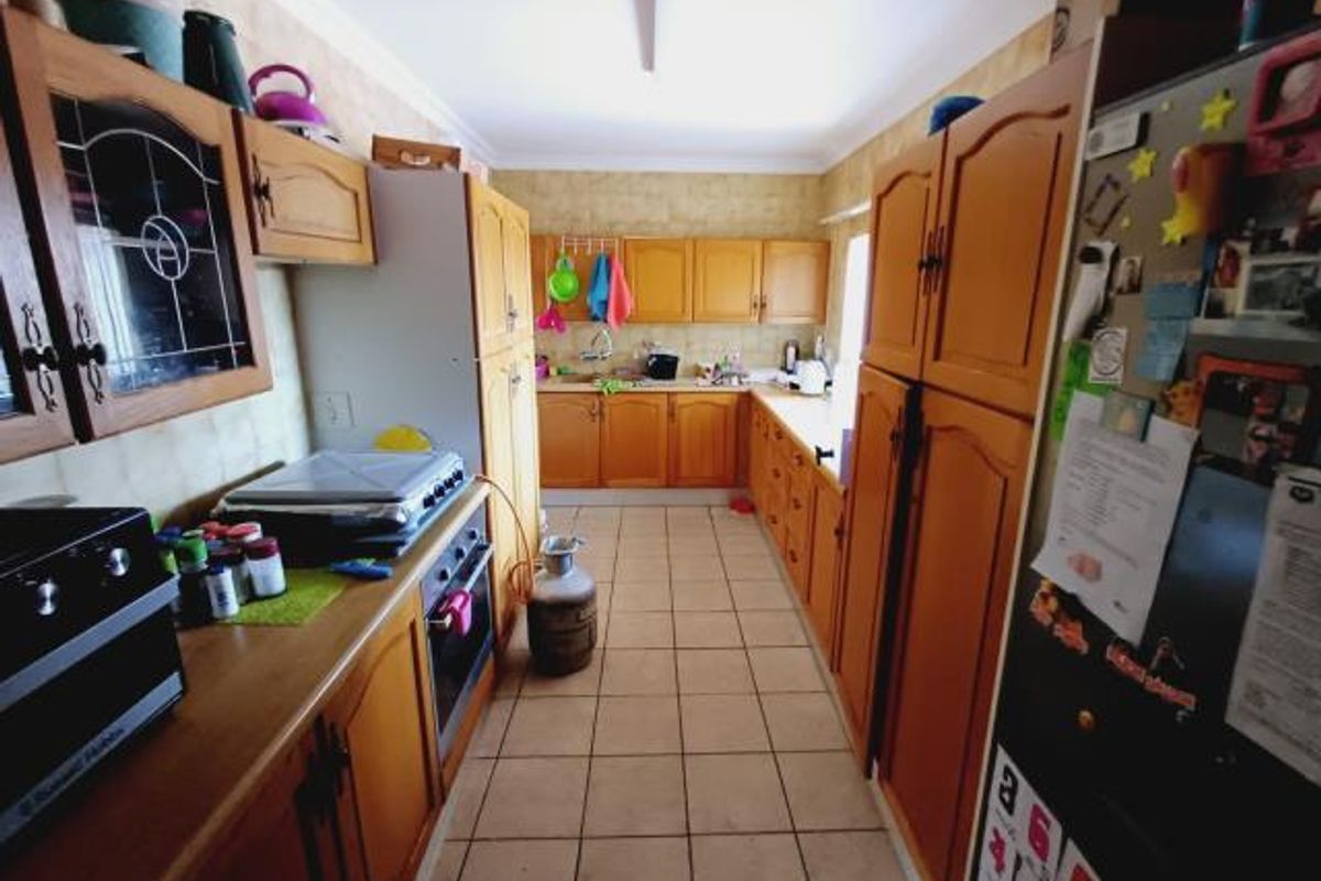 A functional galley-style kitchen featuring traditional wooden cabinetry, tiled flooring, and integrated oven, offering potential for a modern cosmetic update.