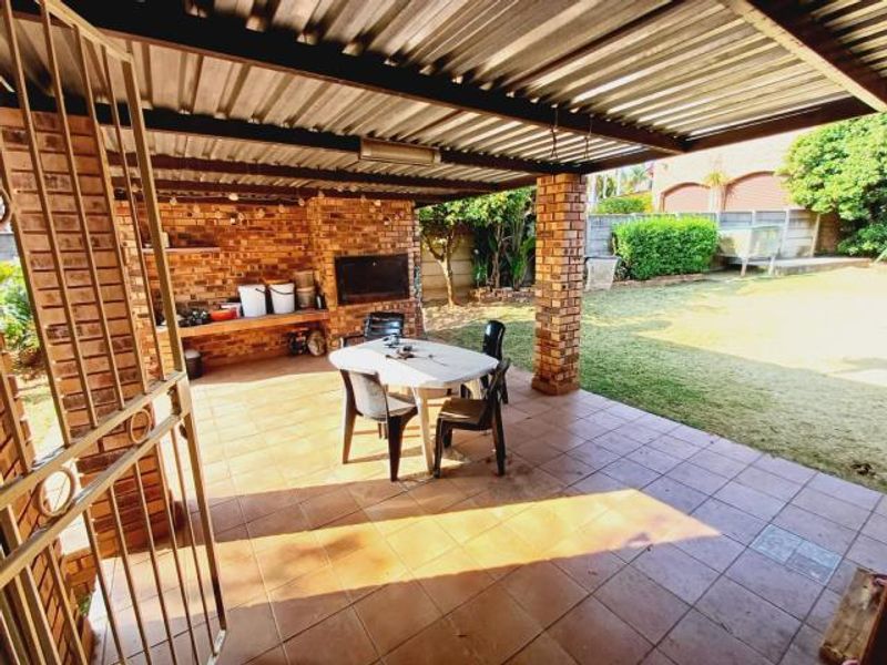 Covered outdoor patio featuring a built-in braai, brick pillars, and tiled flooring, overlooking a private garden area.