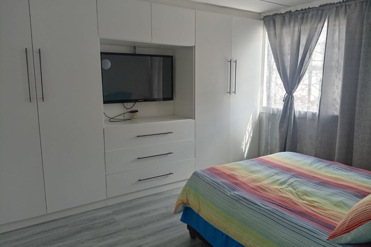 A well-maintained bedroom featuring extensive built-in white cabinetry with integrated storage and shelving, complemented by modern light-toned laminate flooring.