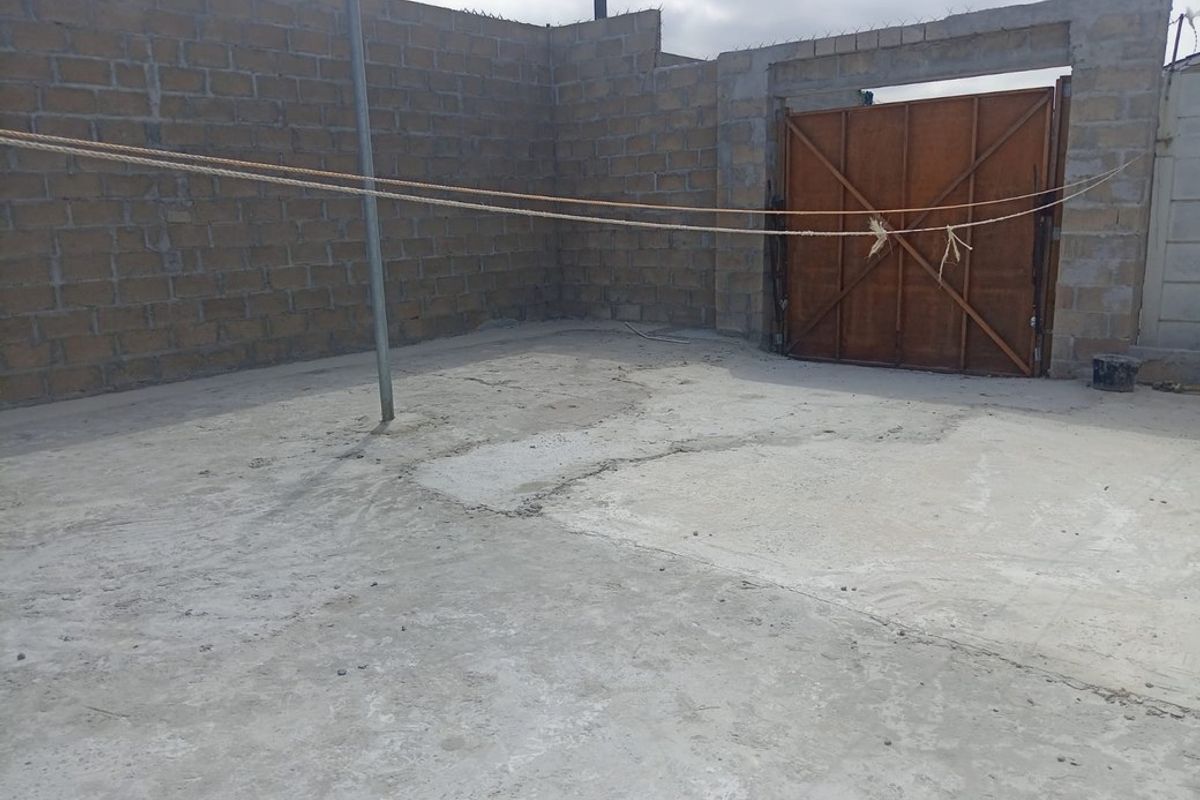 An enclosed outdoor yard area featuring unfinished concrete block walls, a concrete floor, and a metal gate entrance.