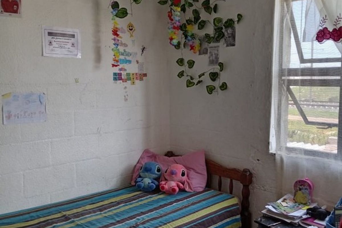 A compact bedroom featuring tiled flooring, a single window with natural light, and exposed block-work walls.