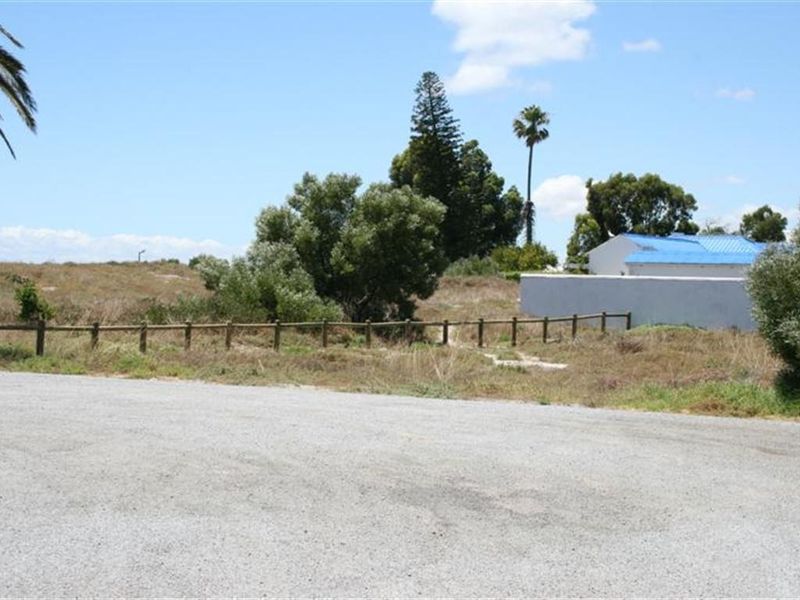 A view of a vacant residential plot featuring a timber post and rail fence, gravel road access, and surrounding natural vegetation.