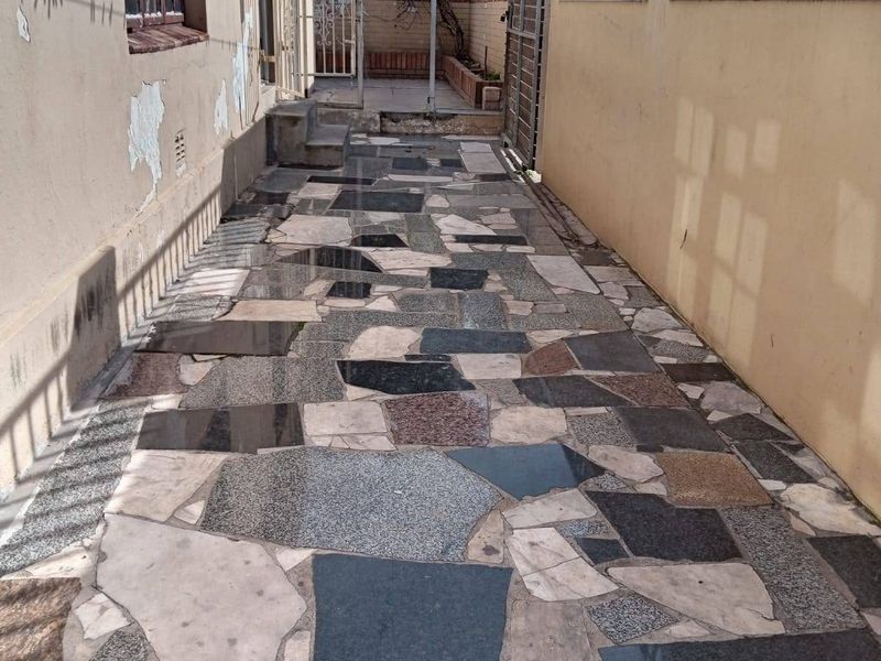 A narrow side exterior walkway featuring a paved stone surface, enclosed by a boundary wall and the side elevation of the house.