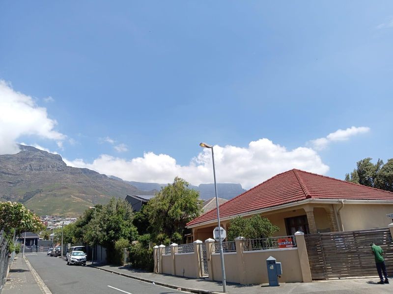 Street view of a residential property featuring a tiled roof, perimeter wall, and mountain backdrop in a suburban setting.