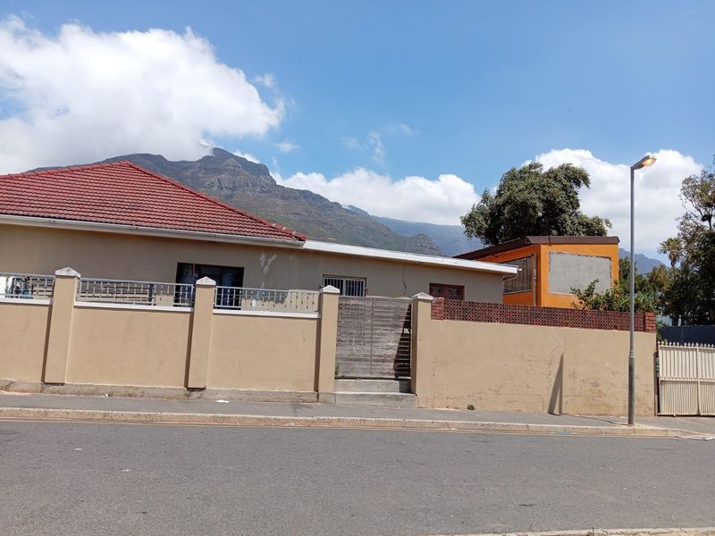 Street view of a residential property featuring a perimeter boundary wall, gated entrance, and tiled roof, set against a mountain backdrop.