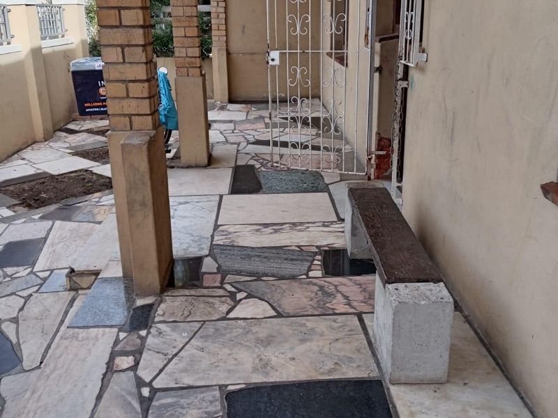 A covered patio area featuring mixed stone crazy paving, brick support columns, and a security gate at the entrance.