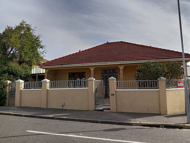 A single-story residential house featuring a tiled roof, covered front porch, and a secure perimeter wall with metal fencing.