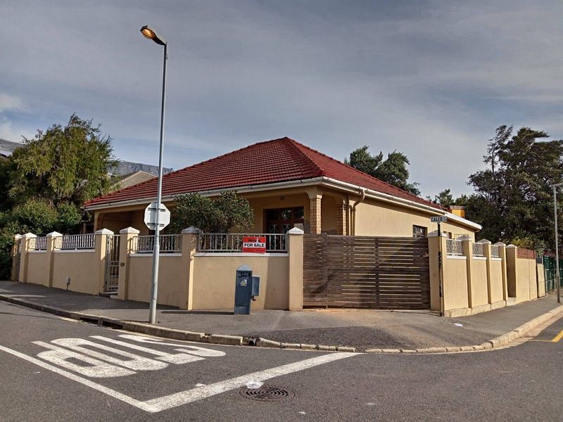 Corner property featuring a tiled roof, perimeter boundary wall with metal fencing, and a wooden driveway gate.
