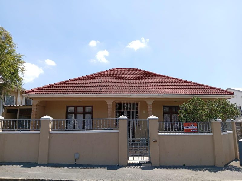 A single-story residential house featuring a tiled hip roof, covered front porch, and a secure perimeter wall with a metal gate.