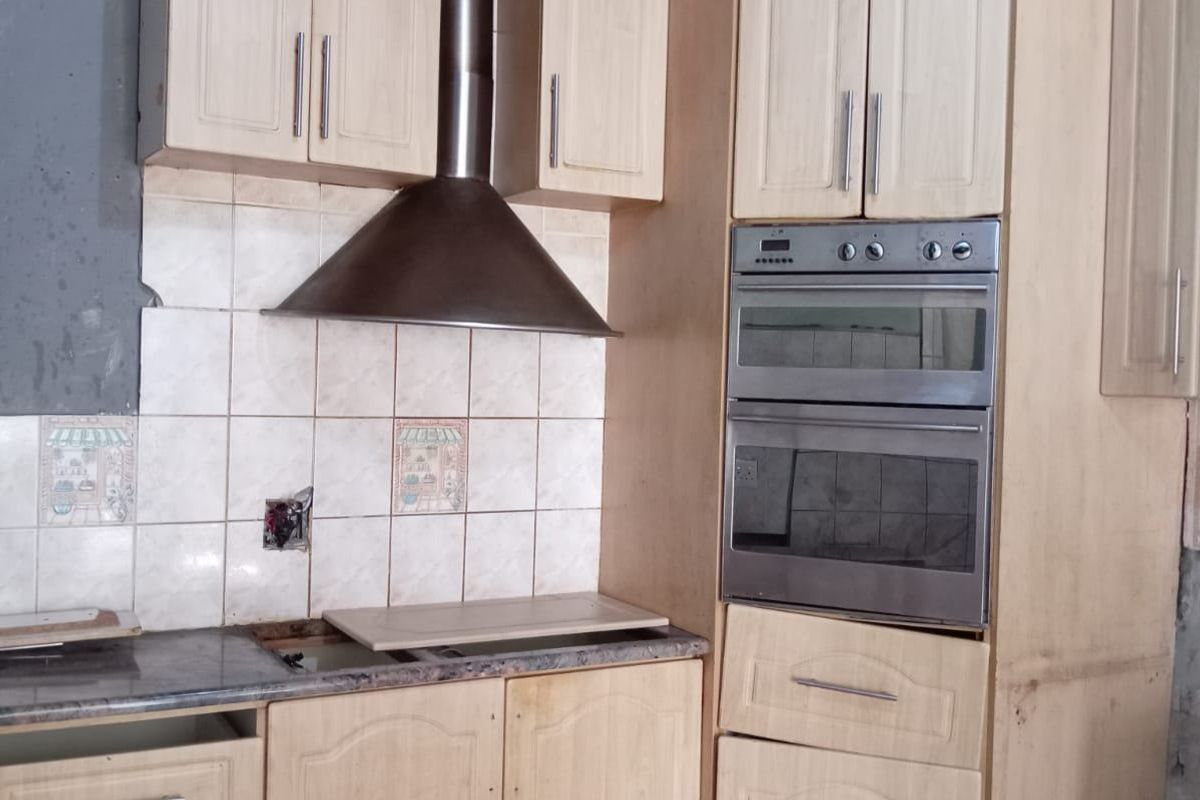 A dated kitchen featuring light wood cabinetry, a built-in double oven, and a stainless steel extractor fan, currently requiring completion and renovation.