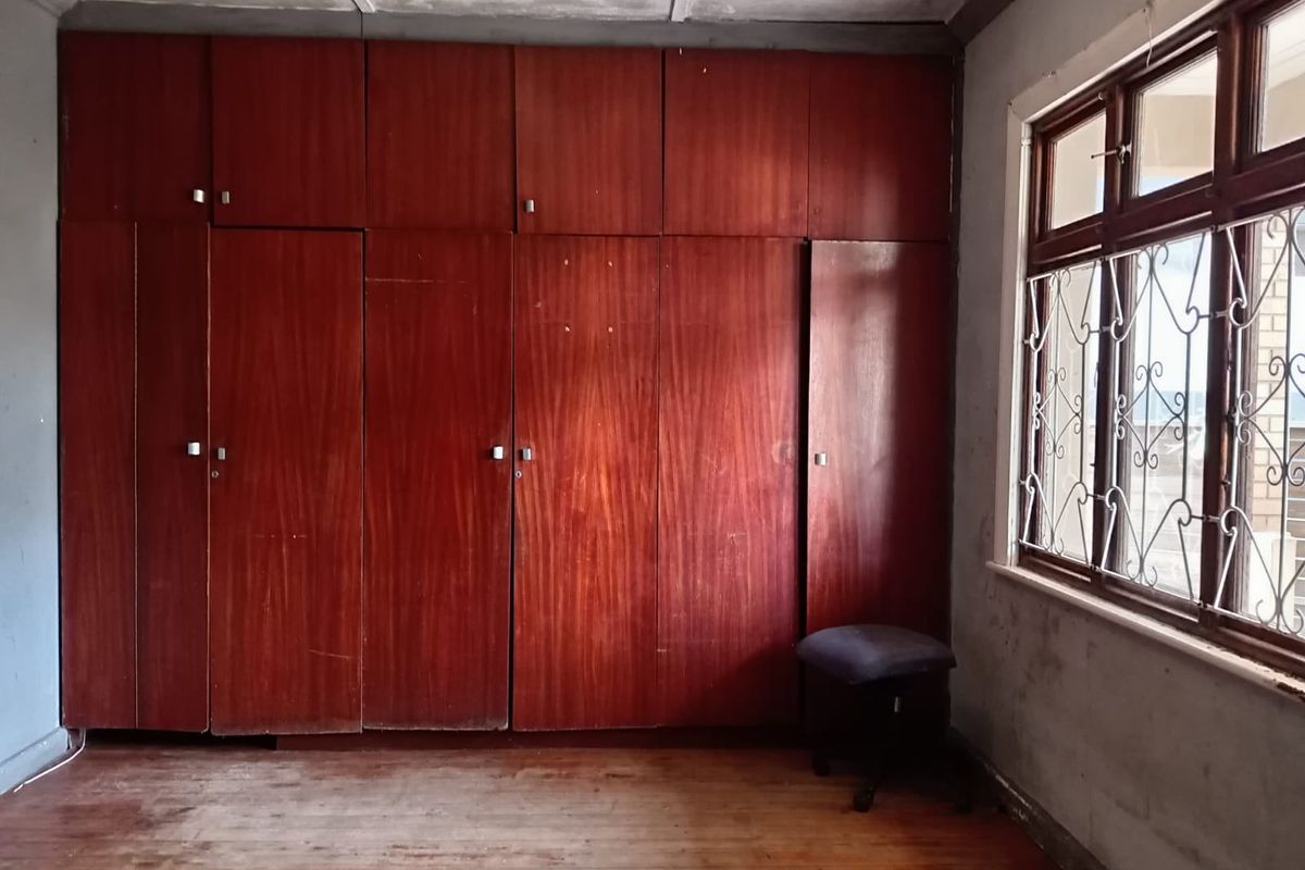 A bedroom featuring extensive floor-to-ceiling built-in wooden cabinetry, timber flooring, and a window with security bars.