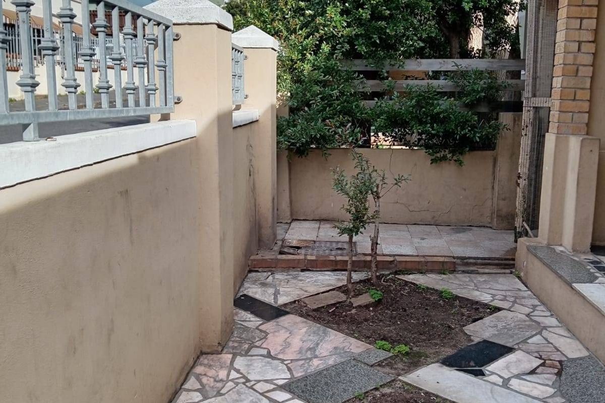 A paved courtyard area featuring a mix of stone tiles and small garden beds, enclosed by a boundary wall with metal railings.