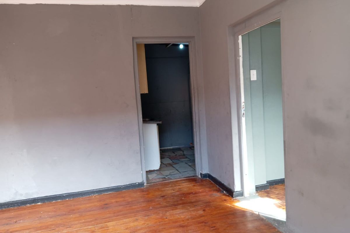 An interior view of a room with polished wooden flooring and grey painted walls, featuring doorways leading to adjacent living spaces.