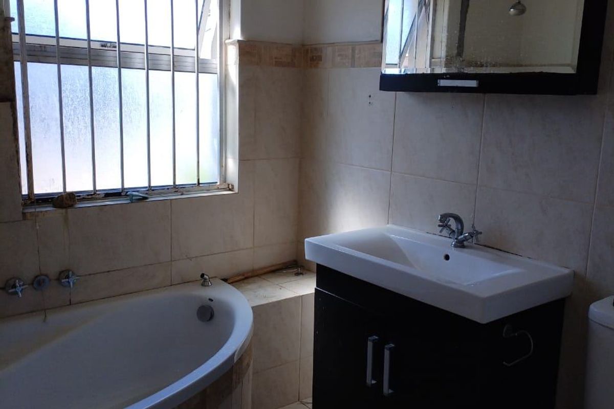 A functional bathroom featuring a built-in bathtub, vanity cabinet with basin, toilet, and wall-mounted mirror cabinet, finished with tiled walls and floors.