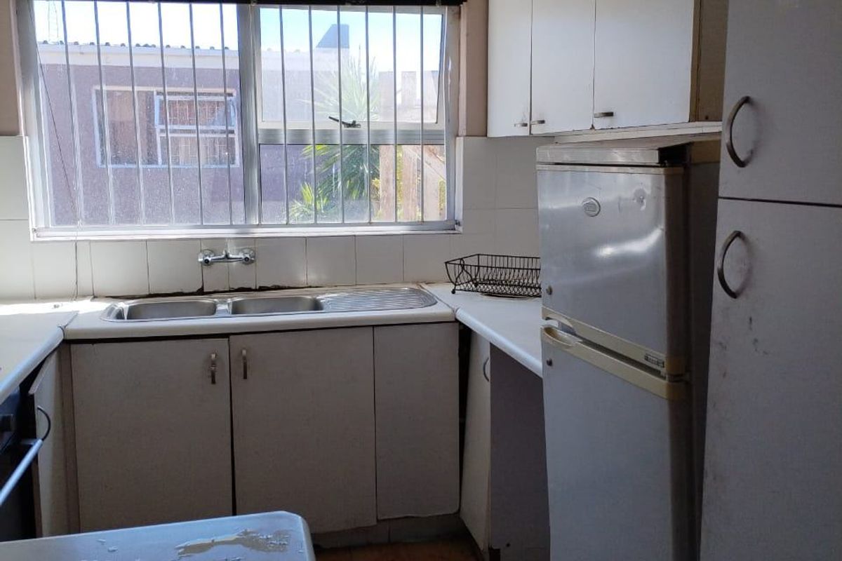 A dated kitchen featuring laminate cabinetry, a double bowl sink, and tiled splashbacks, requiring cosmetic updates to improve functionality and aesthetic appeal.