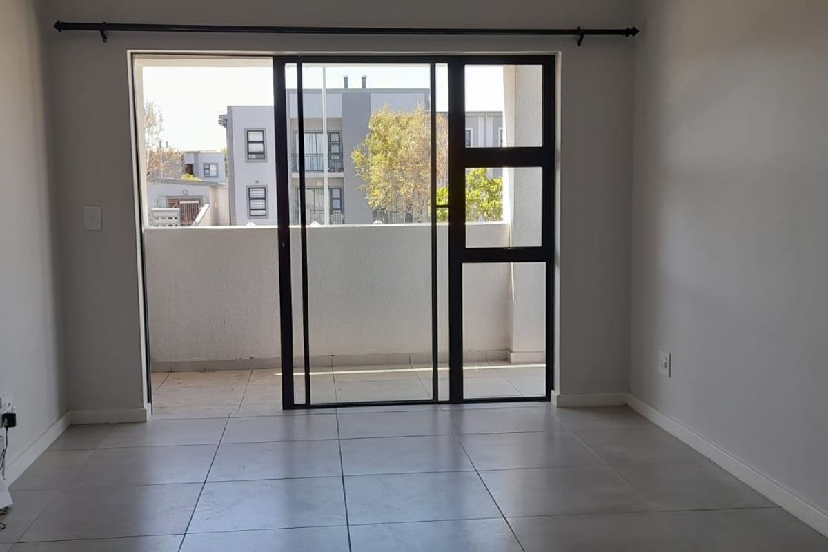 An empty, well-maintained living area featuring neutral tiled flooring and a large sliding glass door providing access to an outdoor balcony.