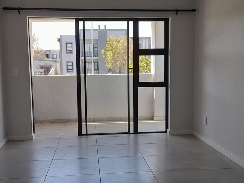 An empty, well-maintained living area featuring neutral tiled flooring and a large sliding glass door providing access to an outdoor balcony.