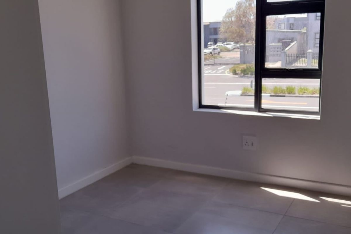 A bright, empty bedroom featuring modern tiled flooring, clean white walls, and a large aluminium-framed window with street views.