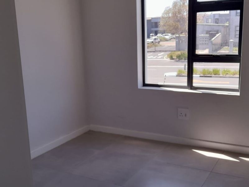 A bright, empty bedroom featuring modern tiled flooring, clean white walls, and a large aluminium-framed window with street views.