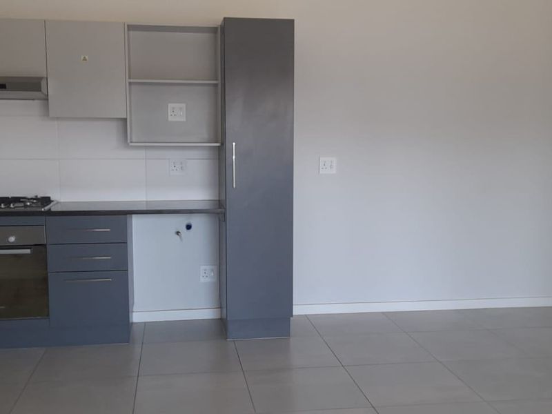Modern kitchen featuring grey built-in cabinetry, a gas hob, built-in oven, extractor fan, and tiled flooring in an open-plan layout.