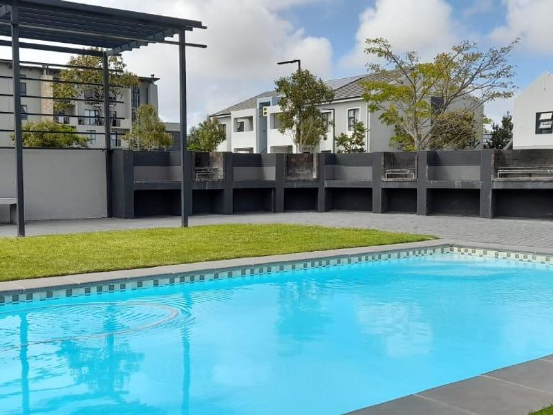 Communal pool area featuring a swimming pool, paved surround, and a covered pergola with built-in braai facilities.