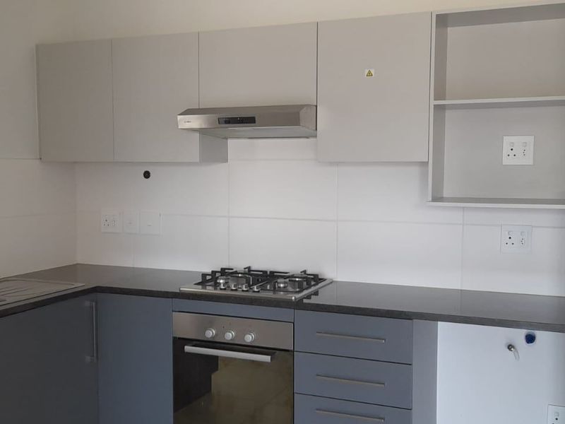 Modern kitchen featuring grey cabinetry, dark laminate countertops, stainless steel sink, gas hob, built-in oven, and extractor fan with a clean tiled splashback.
