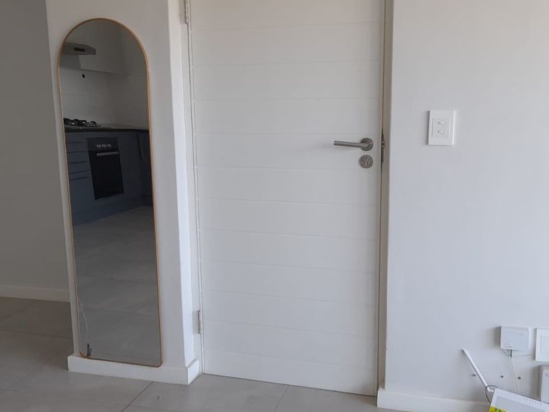 A clean, neutral hallway featuring tiled flooring and a modern internal door, providing access to the adjacent kitchen area.