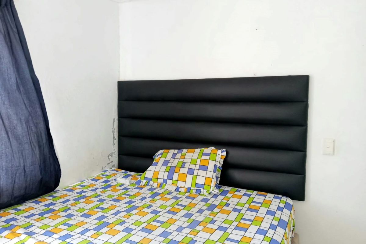 A bedroom interior featuring a wall-mounted headboard, showing visible signs of wall surface wear and paint deterioration.