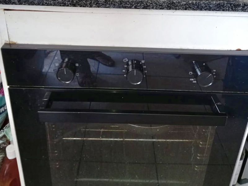 Close-up view of a built-in Defy oven and hob set into a granite countertop, showing signs of wear on the surrounding cabinetry.