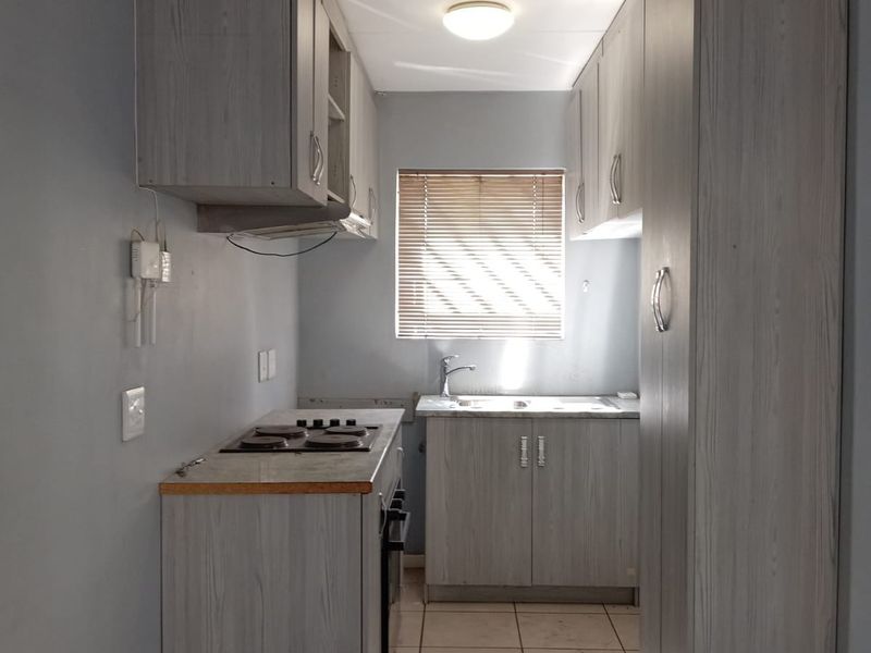 A compact galley-style kitchen featuring light wood-grain cabinetry, a built-in hob and oven, tiled flooring, and a functional sink area.