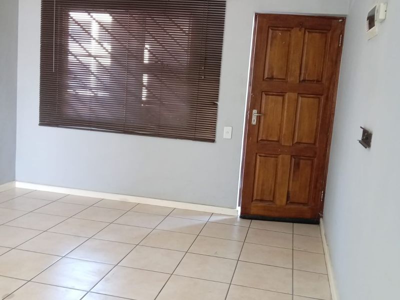 An empty living area featuring neutral tiled flooring, a solid timber entrance door, and window blinds.