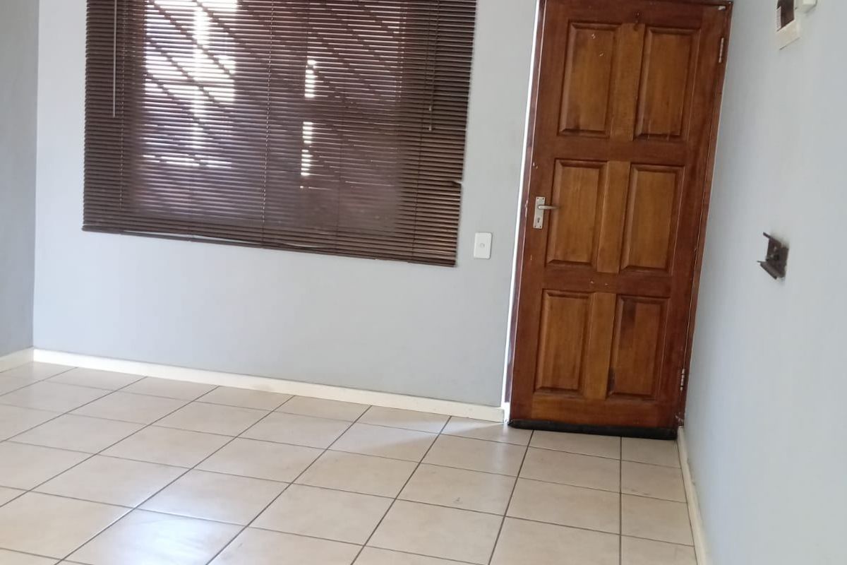 An empty living area featuring neutral tiled flooring, a solid timber entrance door, and window blinds.