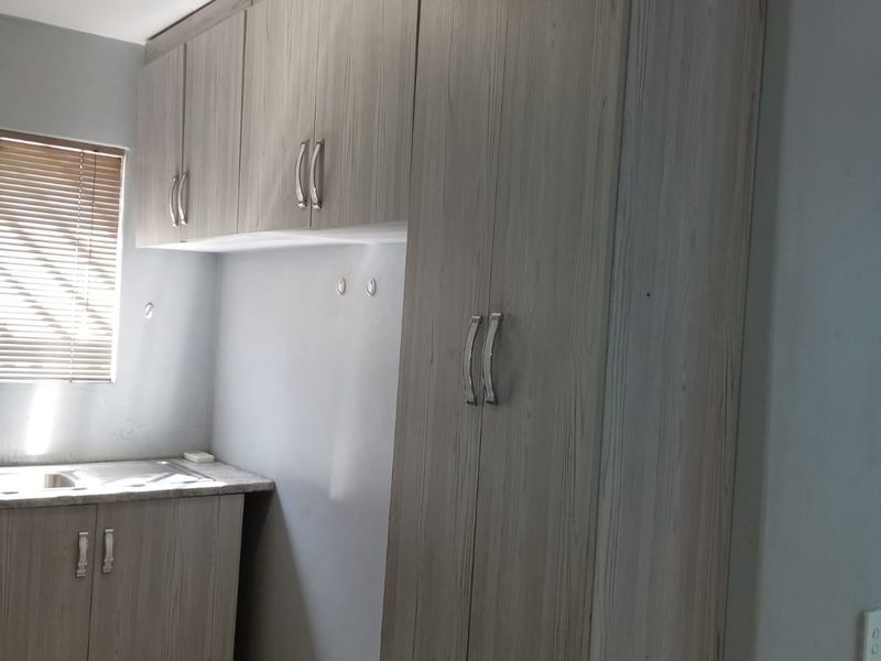 A functional kitchen area featuring light wood-grain built-in cabinetry, laminate countertops, a stainless steel sink, and tiled flooring.